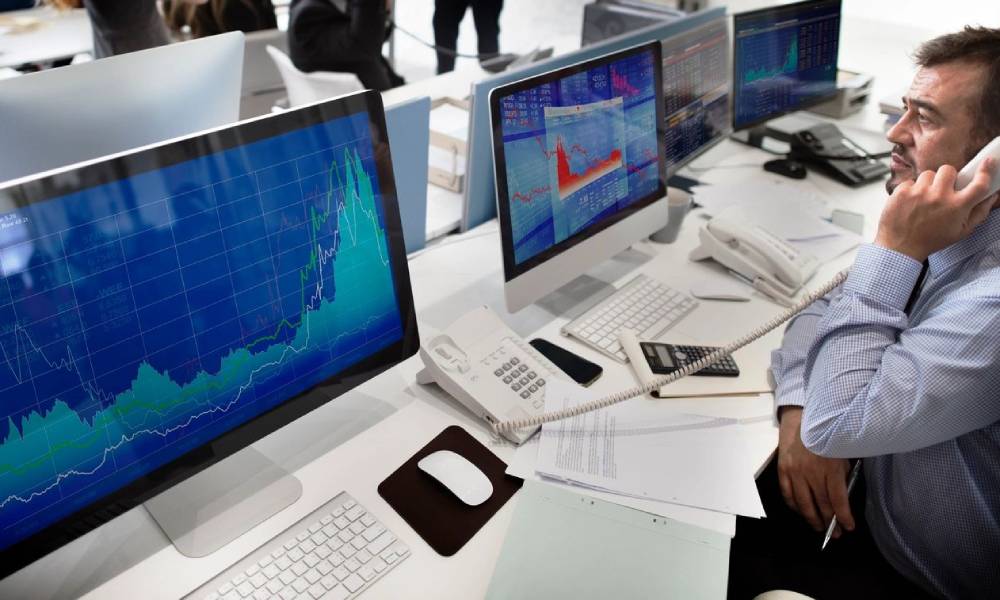 A man sitting at a desk with three computers.