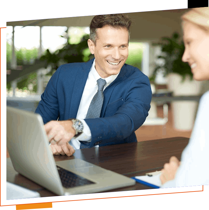 A man and woman shaking hands over a laptop.