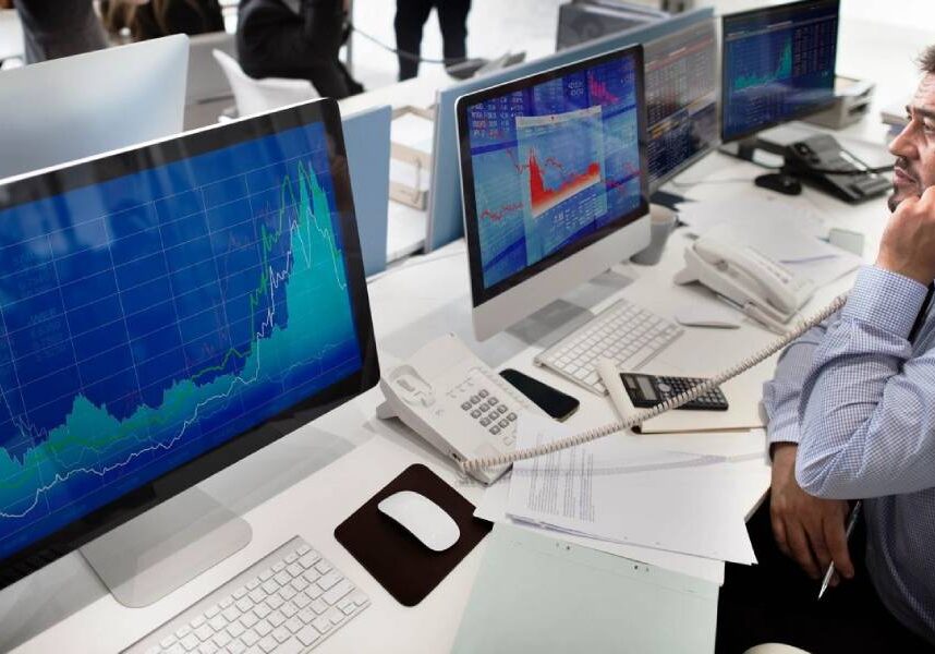 A man sitting at a desk with three computers.